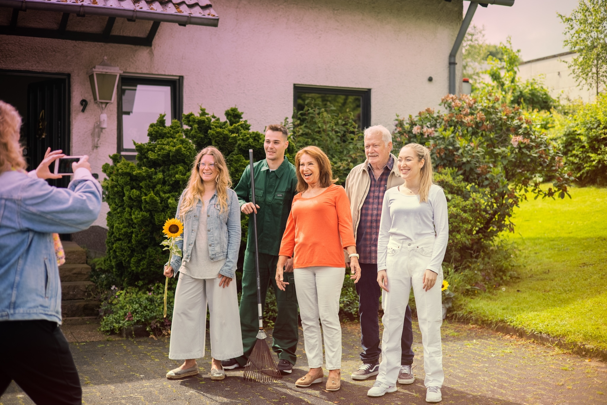 Ein Mädchen macht ein Foto von ihrer Familie zusammen mit dem Gärtner, der gerade gekommen ist, um den Garten in Ordnung zu bringen.