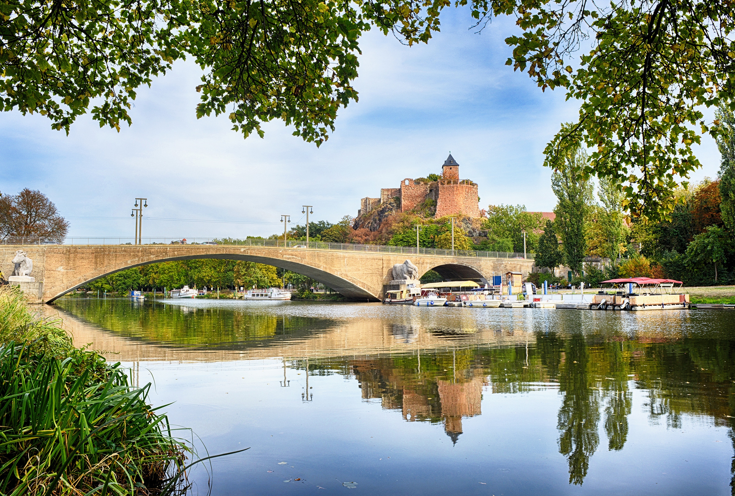 Überblick über einen Touristenort in Halle (Saale) mit der Saale und der Giebichensteinbrücke darüber, mit der Burg Giebichenstein im Hintergrund.